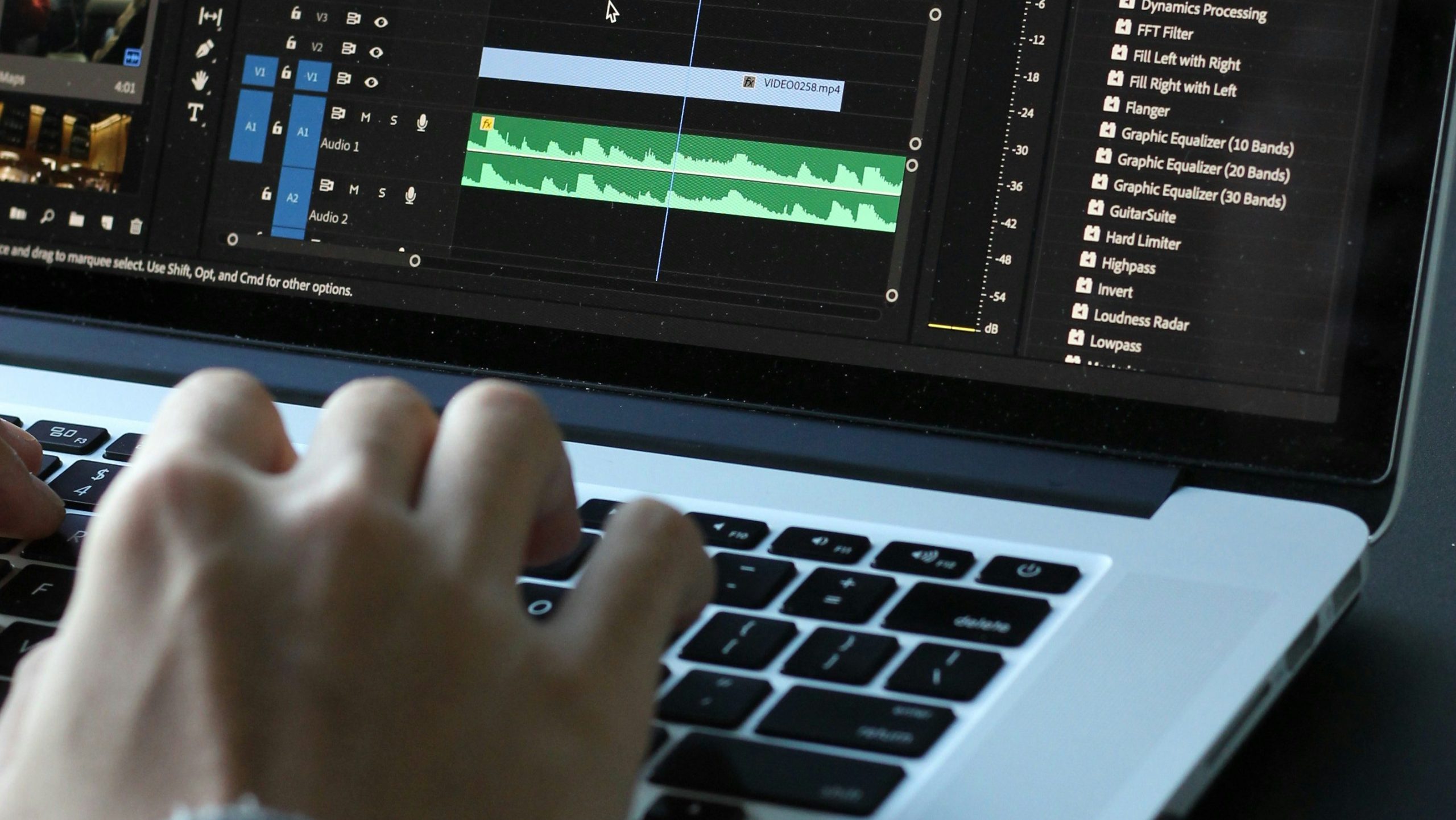 main qui écrit sur un clavier d'ordinateur ouvert sur un logiciel de montage vidéo